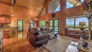 L’intérieur chaleureux d’un chalet avec un plancher en bois, un canapé en cuir, un coin repas et de grandes fenêtres offrant une vue sur l’extérieur.
