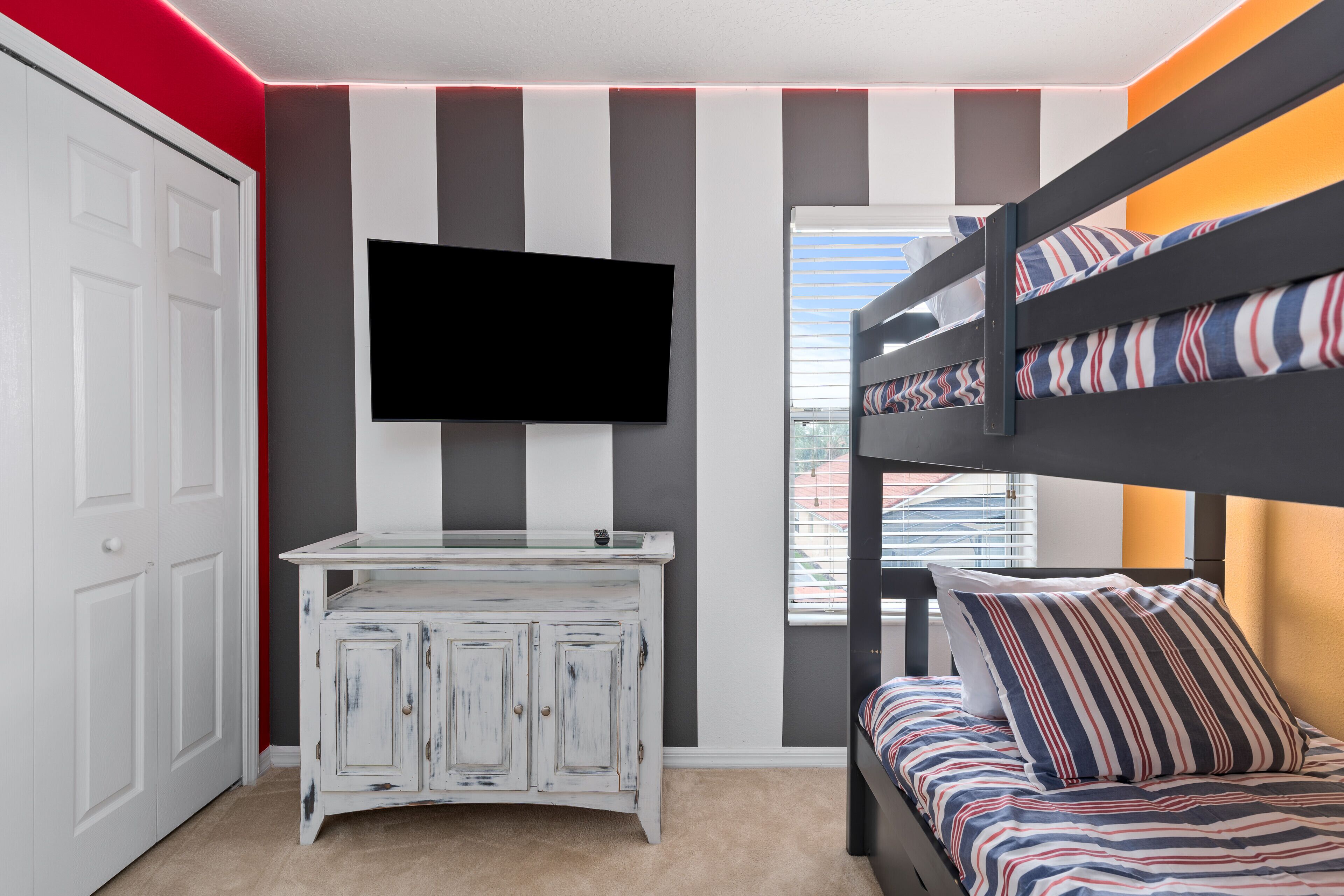 A room with a bunk bed, a TV mounted on the wall, a white cabinet, and a door.
