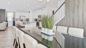 A modern kitchen with white cabinets, a central island, and a dining area with a glass table and white chairs. - Games Room | Kids Bedrooms | Screened Pool with Water Views (Kissimmee)