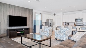 A modern living room with a flat-screen TV, leather sofa, patterned armchairs, and a glass coffee table. - Games Room | Kids Bedrooms | Screened Pool with Water Views (Kissimmee)
