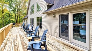 Een houten terras met blauwe Adirondack-stoelen, een barbecue en een glazen deur naar een overdekt terras.