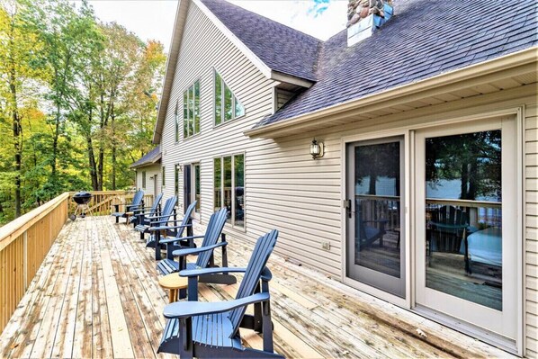 A wooden deck with blue Adirondack chairs, a barbecue grill, and a glass door leading to a covered patio.