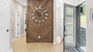 Un pasillo con un gran reloj de pared de madera, puertas blancas y una puerta de cristal que da al exterior.