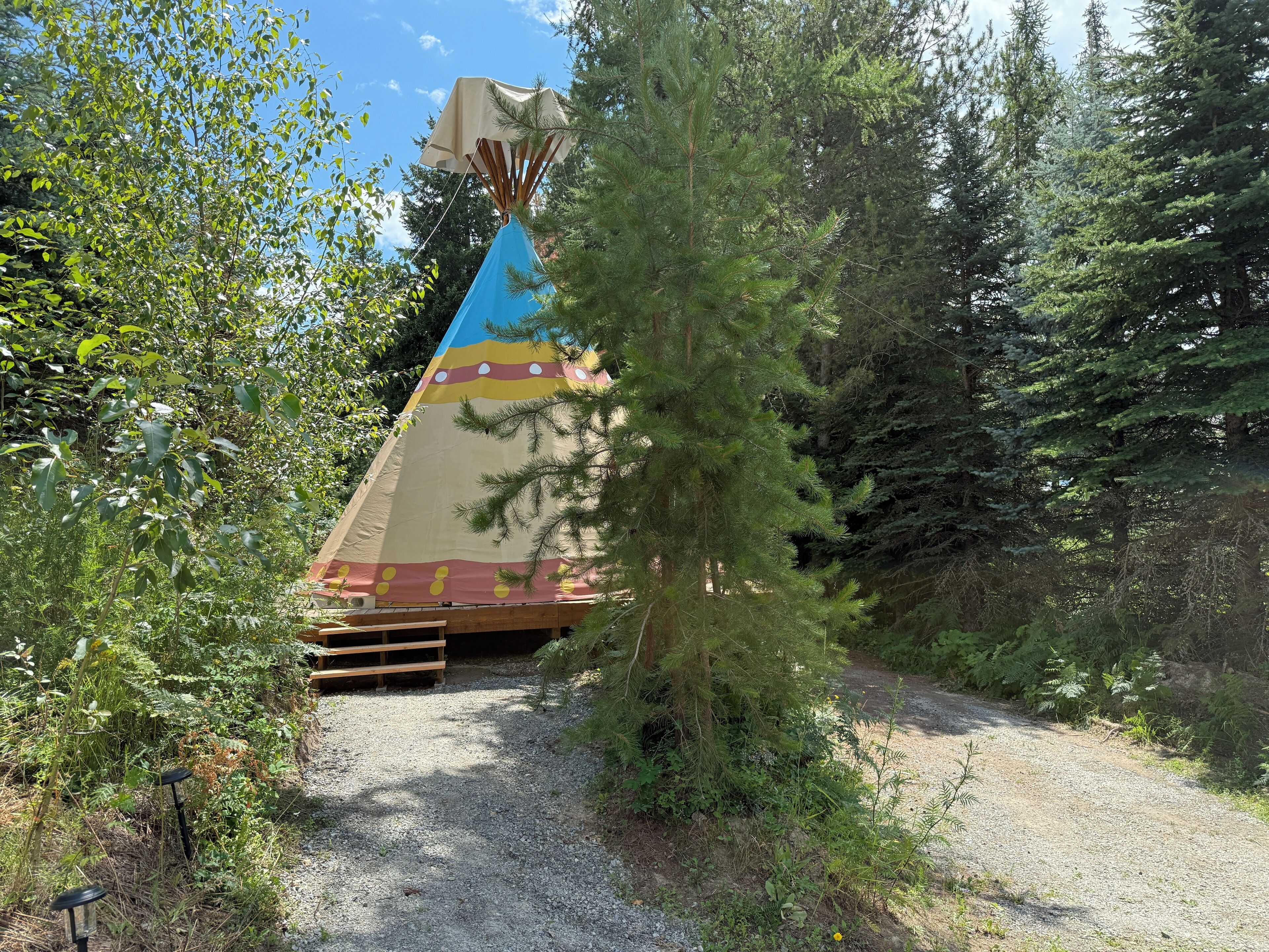 A colorful teepee-like structure in a forested area with a gravel path leading to it.