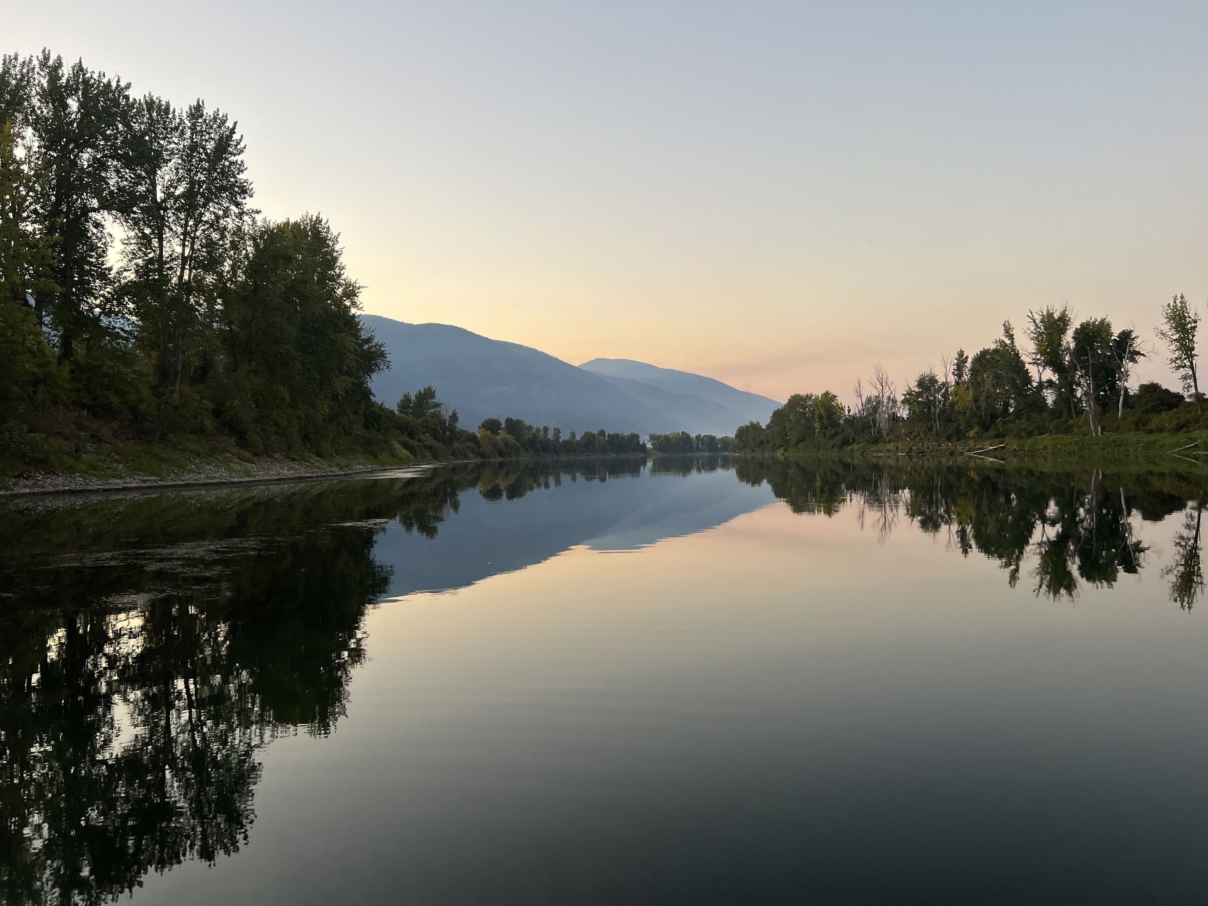 Un río tranquilo con reflejos de árboles y montañas en el agua.