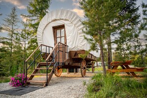 A covered wagon with a wooden ramp and a picnic table in a forested area. - North Haven Campground (Bonners Ferry)
