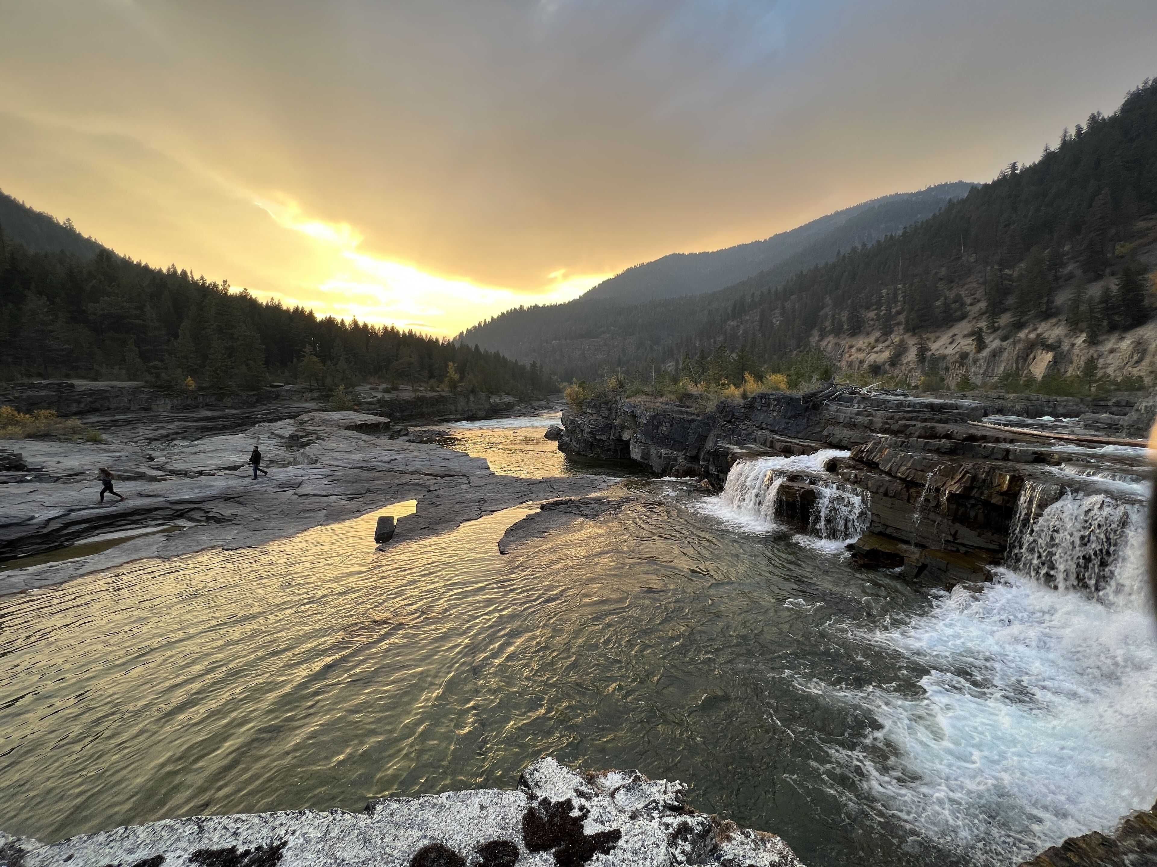 A river with a waterfall, surrounded by forested mountains.