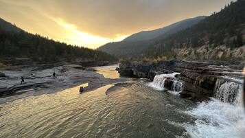 A river with a waterfall, surrounded by forested mountains.