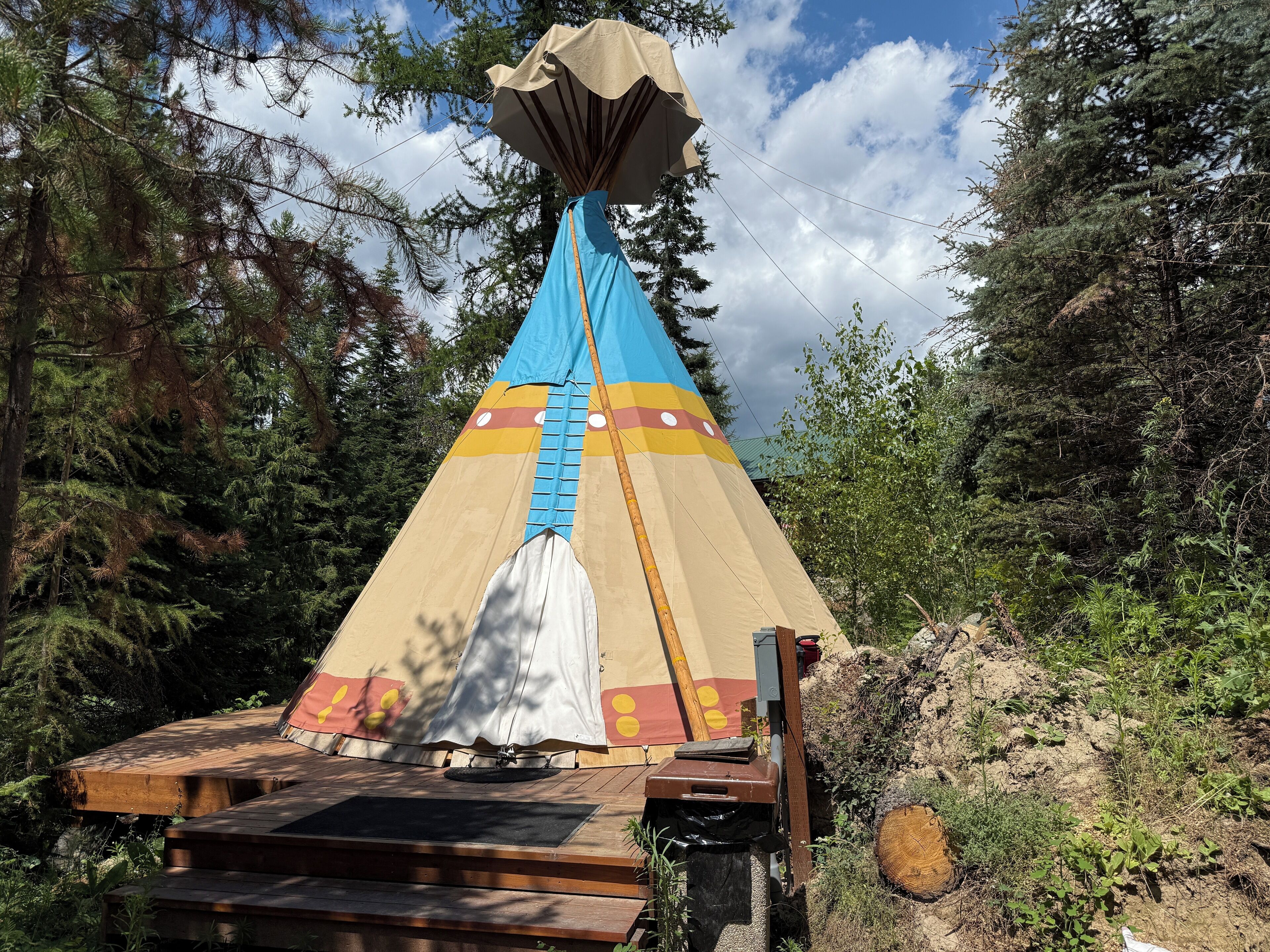 A large, colorful tent with a blue and beige design, set up on a wooden platform in a forested area.