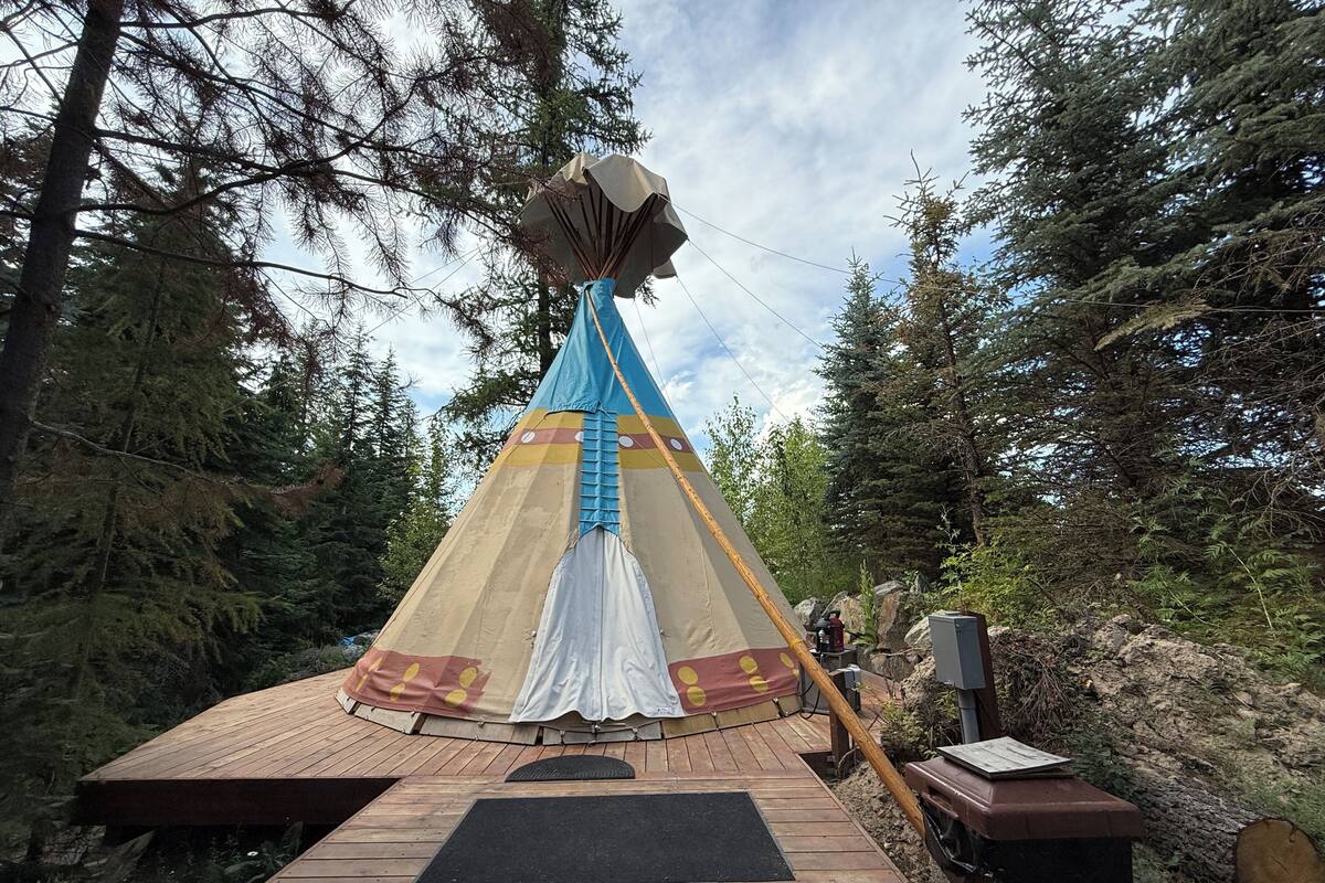 A large, multi-colored teepee with a wooden deck in a forested area.