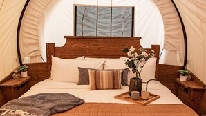 Una habitación con carpa, una cama de madera, una mesita de noche, una lámpara colgante y una ventana.