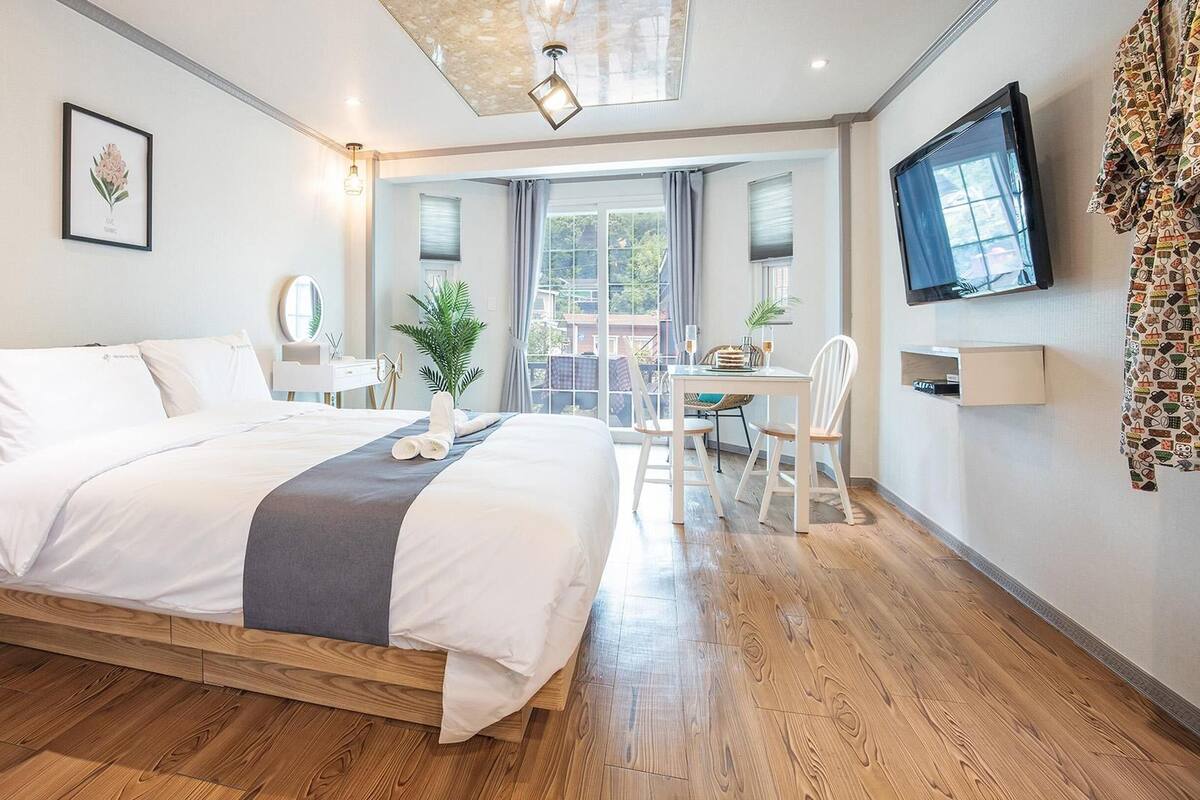A hotel room with a large bed, a desk with chairs, a TV, and a window with curtains.