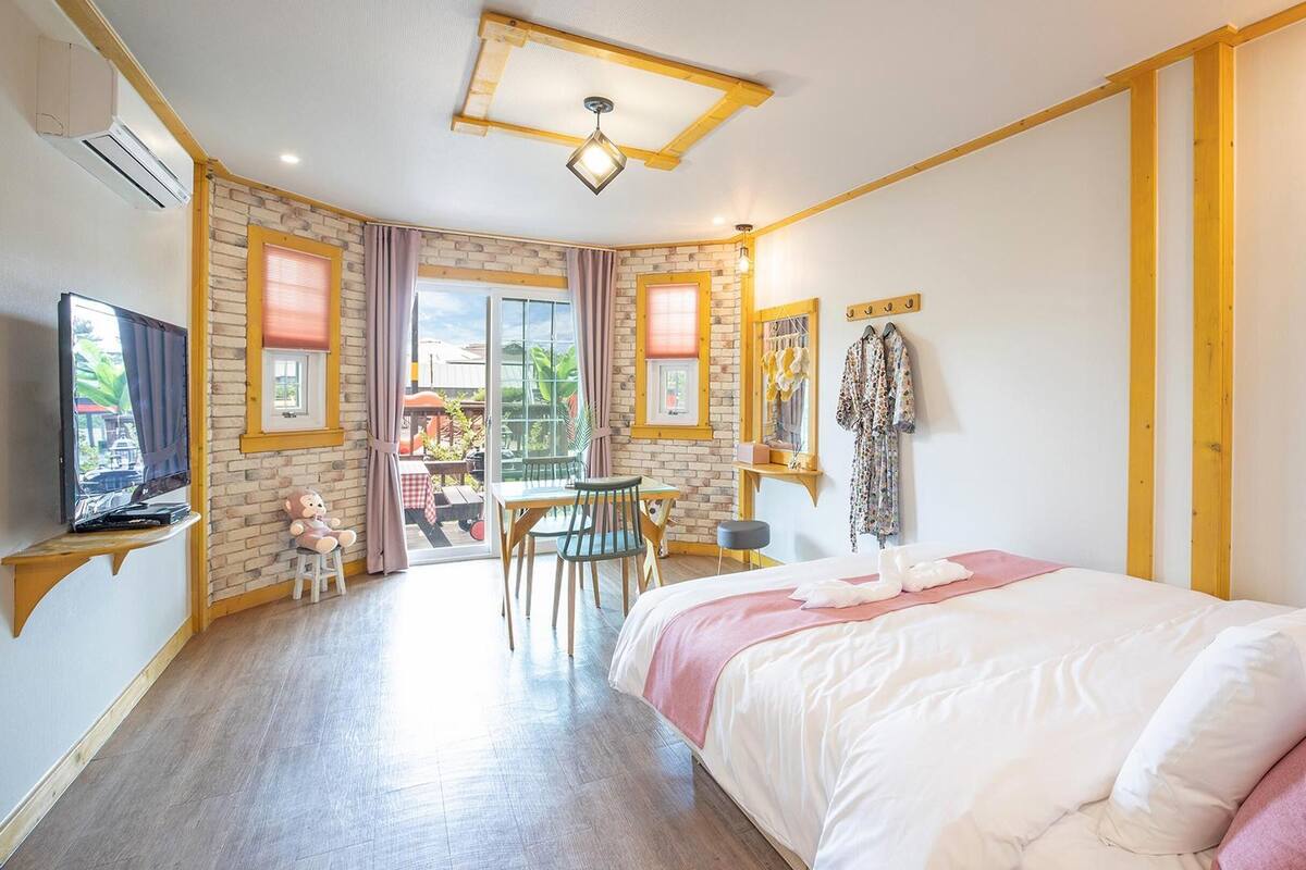 A hotel room with a bed, a desk, a chair, a TV, and a window with curtains.
