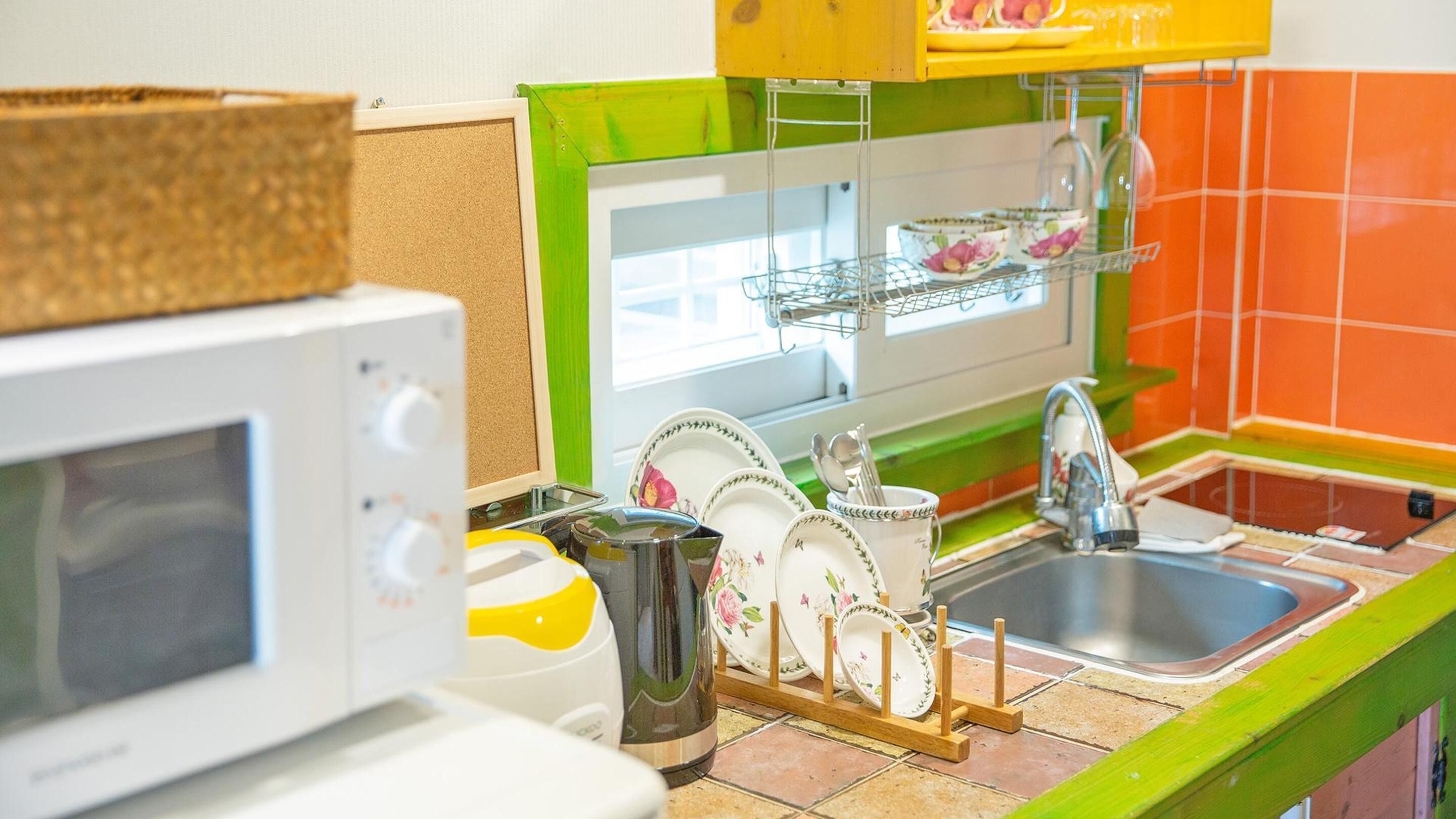 Una cocina con microondas, pileta y escurreplatos.