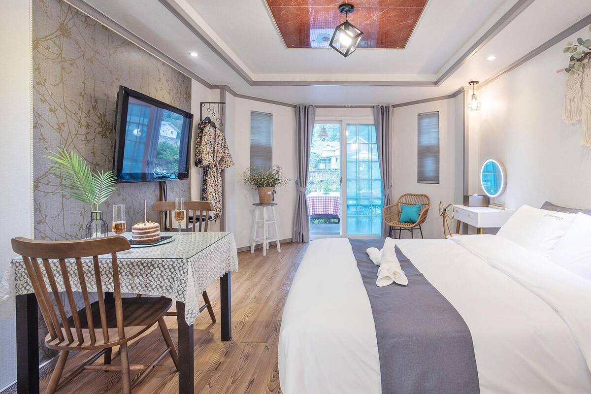 A hotel room with a bed, a desk with a chair, a TV, and a view of the outdoors.