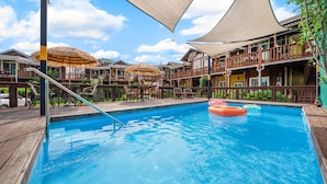 A swimming pool with wooden deck and lounge chairs, surrounded by buildings with balconies and thatched umbrellas. - Gyeongju Papaya Aegyeondongban Pension (Gyeongju)