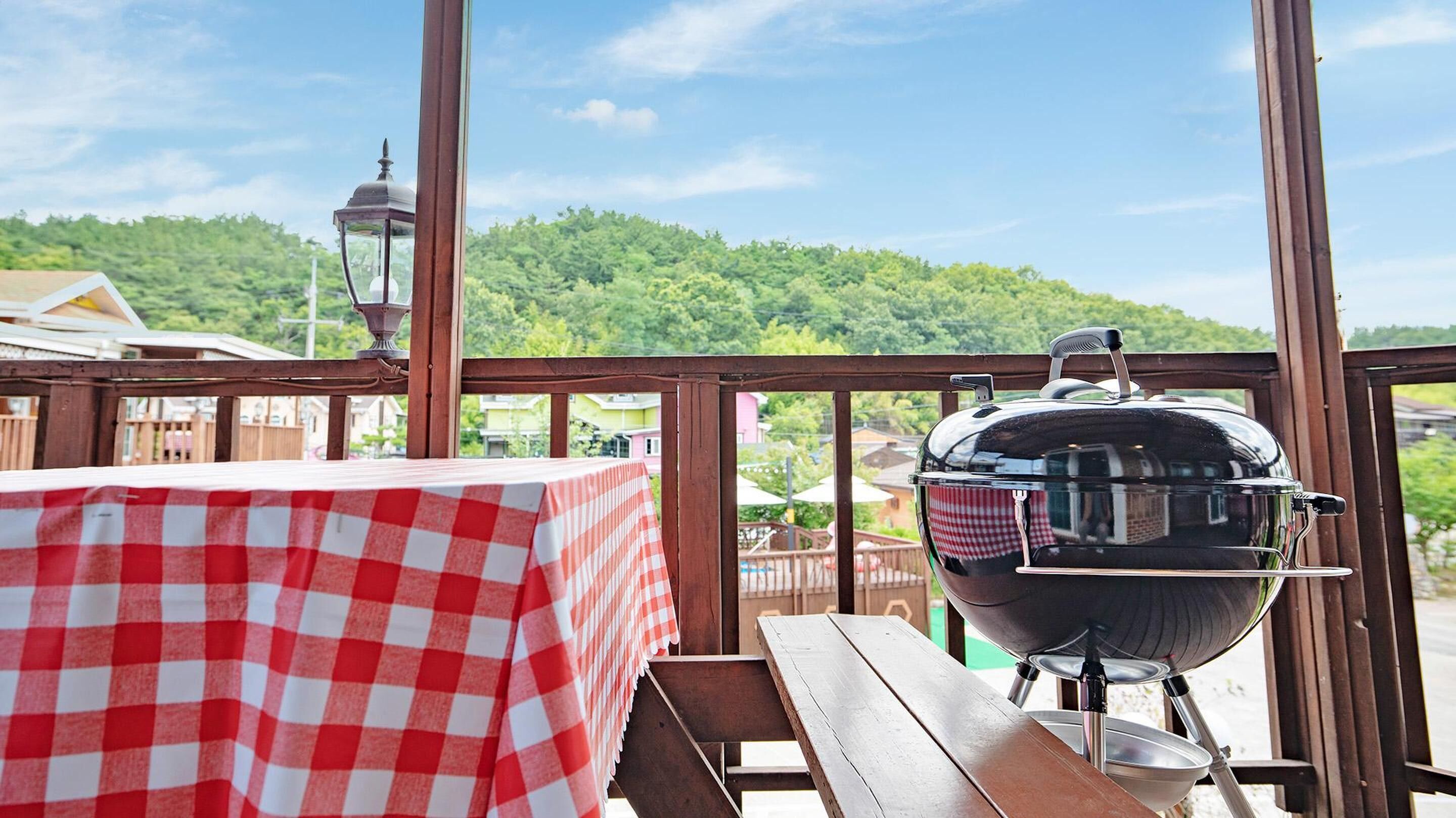 A wooden deck with a checkered tablecloth and a barbecue grill.