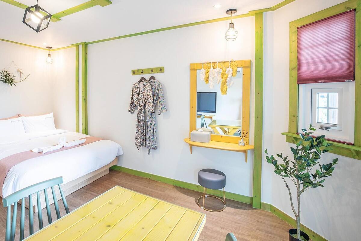 A bedroom with a bed, bedside table, TV, and a small stool.