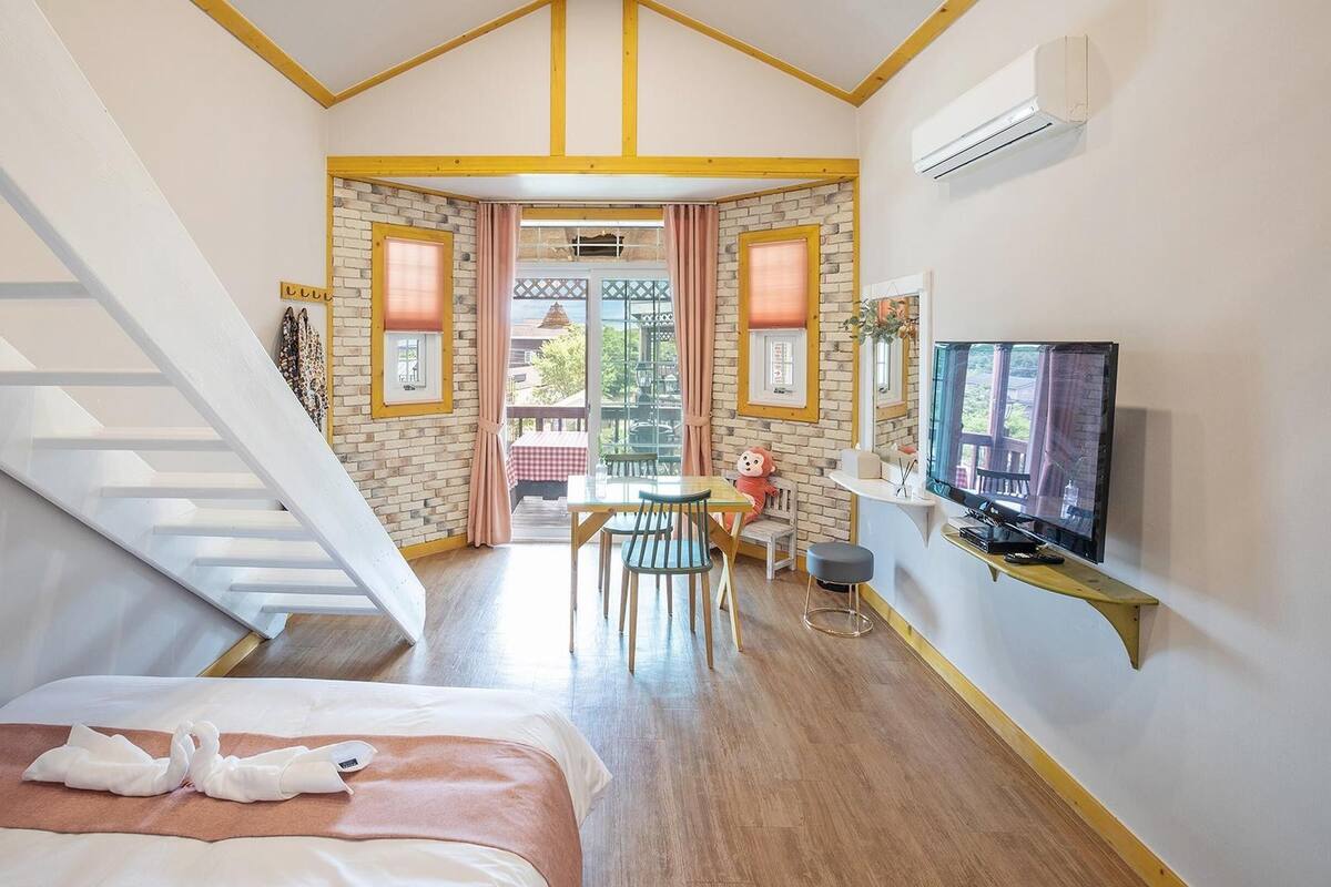 A hotel room with a bed, a TV, a dining area, and a staircase.