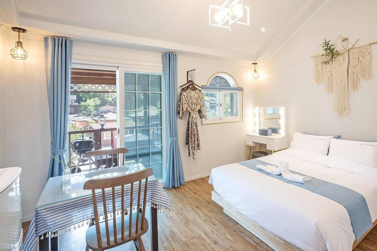 A bedroom with a bed, a desk, a chair, a window, and a balcony.