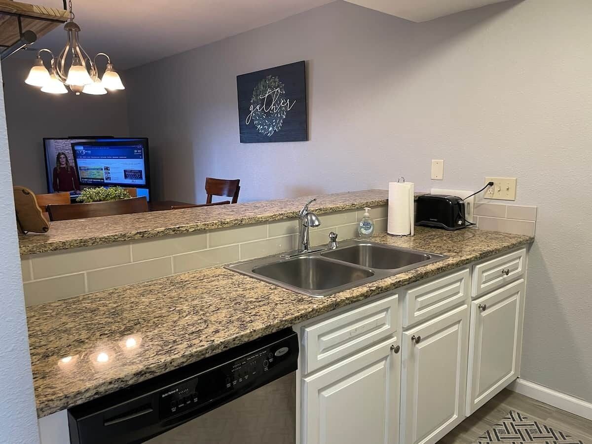 A kitchen with granite countertops, white cabinetry, a double sink, and a dishwasher.