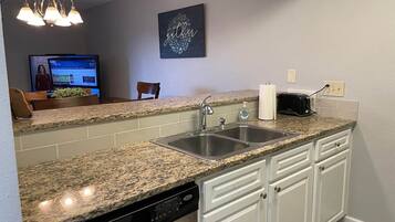 A kitchen with granite countertops, white cabinetry, a double sink, and a dishwasher.