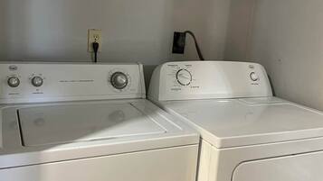 A laundry area with two white front-loading washing machines, a power outlet, and a metal shelf above.
