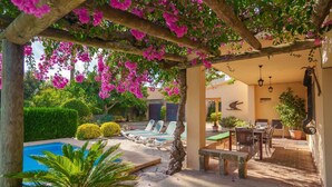 A covered outdoor area with a pool, lounge chairs, and a dining table.