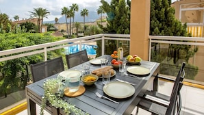 Ein Esstisch auf einem Balkon mit Stühlen, einer Karaffe, Gläsern, Tellern und Schüsseln voller Speisen.