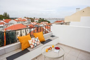 A balcony with a view of a cityscape, a round table with breakfast items, and orange cushions.