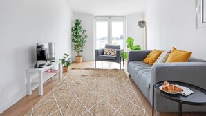 A modern living room with a sofa, a TV, a small table, and a large window. - One bedroom Apt | Almada | Balcony w/River Views by Lisbeyond (Almada)