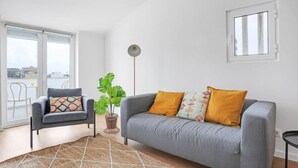 A modern living room with a grey sofa, a patterned armchair, a large green plant, and a floor lamp. - One bedroom Apt | Almada | Balcony w/River Views by Lisbeyond (Almada)