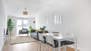 A modern living room with a sofa, a dining table with chairs, and a large window. - One bedroom Apt | Almada | Balcony w/River Views by Lisbeyond (Almada)