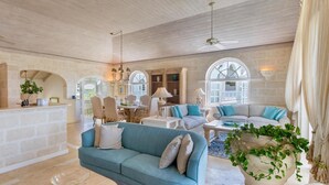 A spacious living area with a stone wall, a blue sofa, and a large window. - Forest Hills 23 | Beach View - Located in  Wonderful Saint James with House Cleaning Included (Saint James)