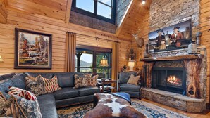 A cozy cabin interior with a large fireplace, wooden walls, a leather sofa, and a mounted deer head. - Elegant Mountain Lodge with Beautiful Sunsets (Vilas)