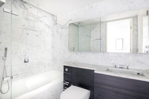 Un baño moderno con ducha envuelta en vidrio, una bañera blanca, un tocador negro con lavamanos y un espejo grande sobre el tocador.