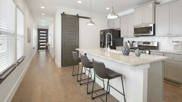 A modern kitchen with a central island, bar stools, stainless steel appliances, and pendant lighting.