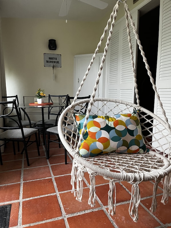 A room with a hanging chair, a dining table with chairs, and a sign on the wall.