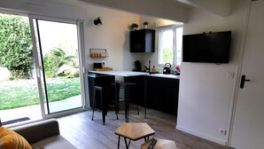 A modern living room with a grey sofa, a small wooden table, and a kitchen area with a black countertop and cabinets. - L'Annexe - Studio 2/4 pers - Private pool (Les Sables-d´Olonne)