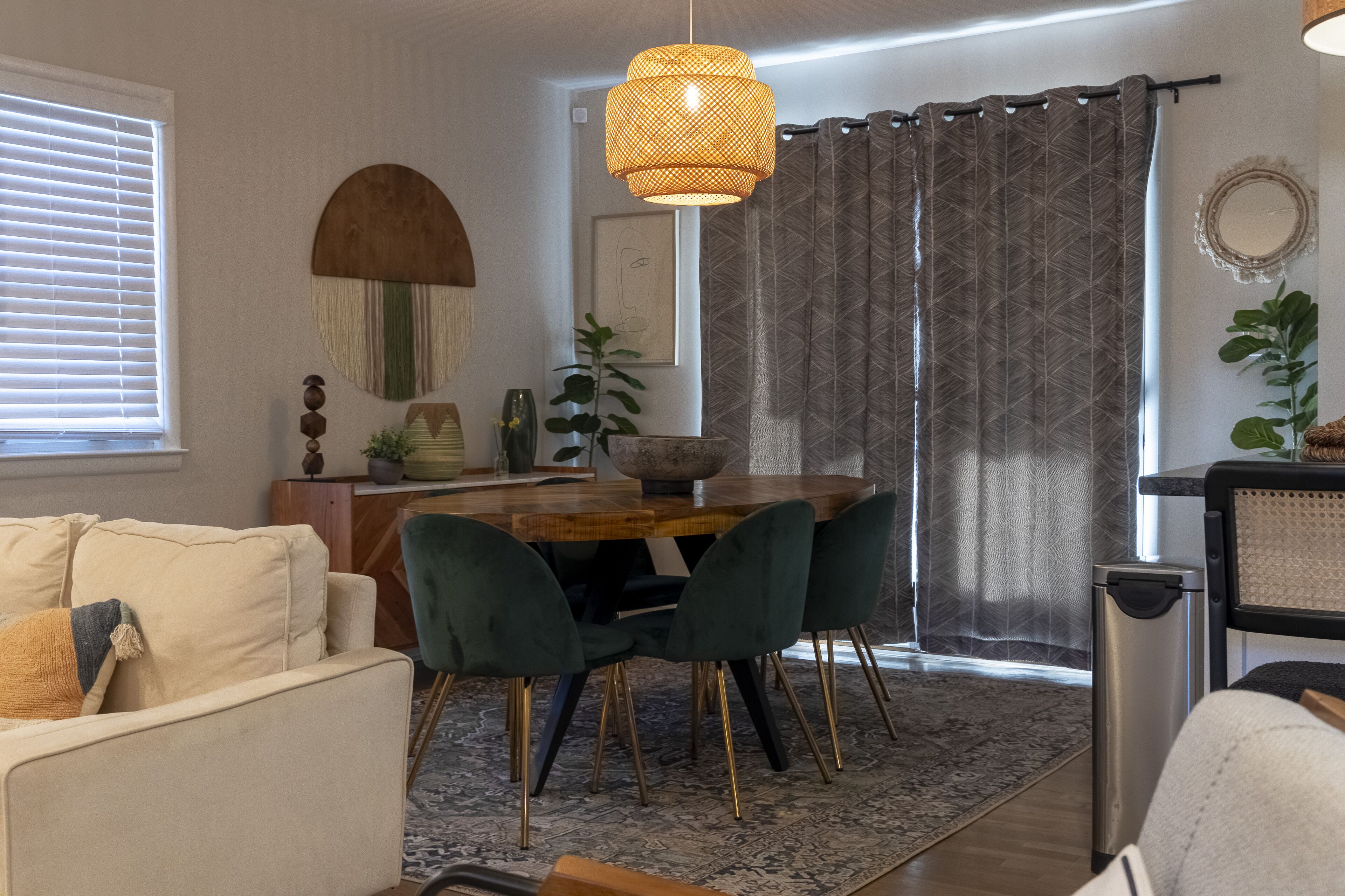 Een eetgedeelte met een houten tafel, groene fauteuils en een geweven hanglamp.