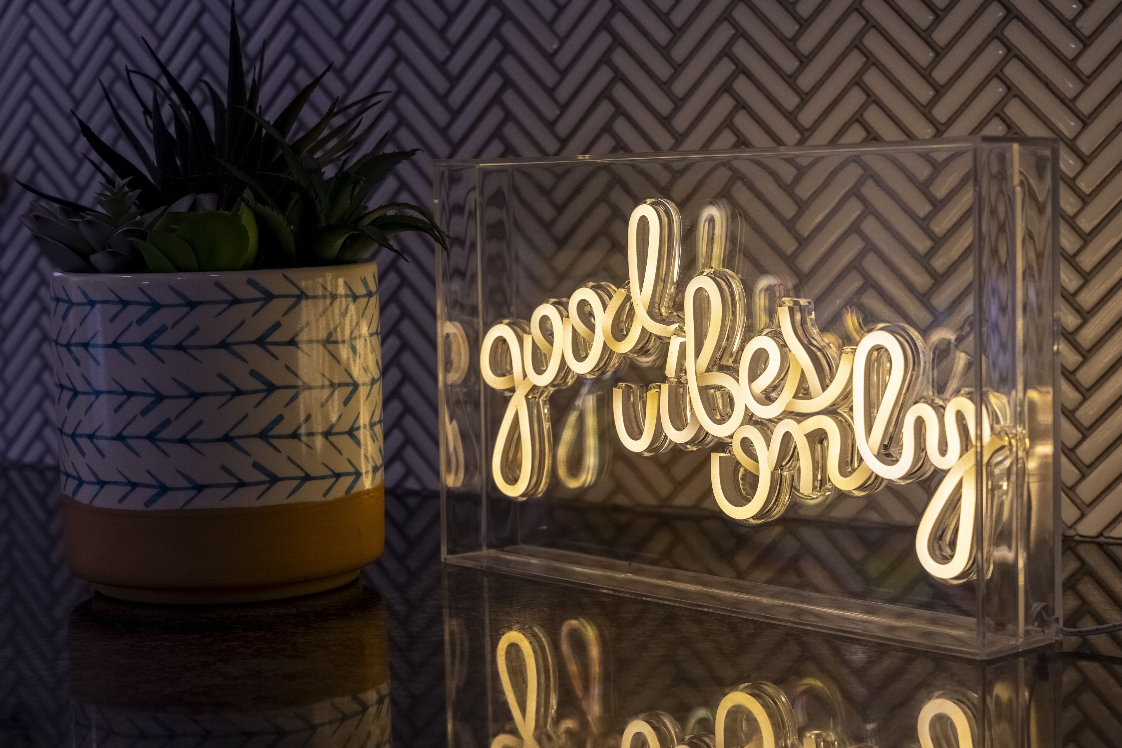 A potted plant with a geometric pattern and a clear acrylic sign with the text "good vibes only" illuminated from within.
