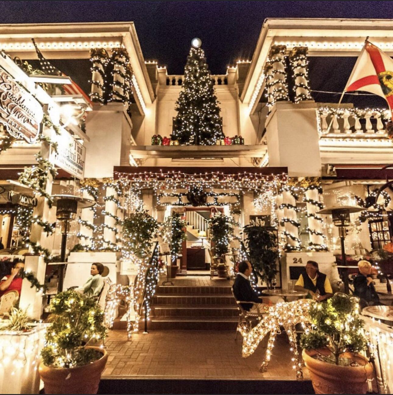 Um edifício com árvore de Natal e luzes, uma escadaria que leva à entrada e uma bandeira.