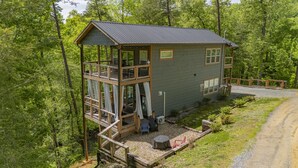 A cabin with a deck, a covered outdoor seating area, and a gravel driveway.