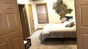 Un dormitorio con cama, un tapete grande en la pared, una ventana con persianas y una puerta.