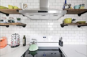 A kitchen with white tiled backsplash, stainless steel range hood, and wooden shelves holding dishes and jars.