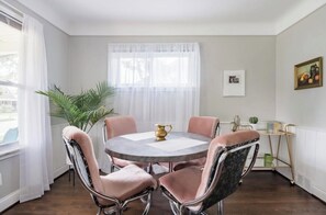 A dining area with a round table, four chairs, a potted plant, and a window with sheer curtains.