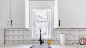 Una cocina con armarios blancos, un lavamanos de acero inoxidable, una ventana, un tostador y un dispensador de jabón.