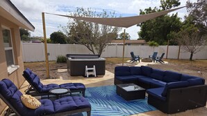 An outdoor patio with a sectional sofa, lounge chairs, a hot tub, and a covered area with a patio table and chairs. - Newly renovated outdoor space, hot tub, fire pit,minutes from the beach. (Largo)