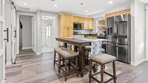 A modern kitchen with wooden cabinets, a stainless steel refrigerator, and a dining area with stools. - Newly renovated outdoor space, hot tub, fire pit,minutes from the beach. (Largo)