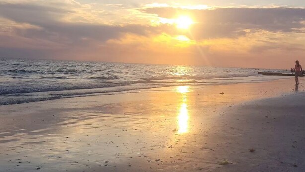 A beach with a sunset, calm waves, and a person walking. - Newly renovated outdoor space, hot tub, fire pit,minutes from the beach. (Largo)